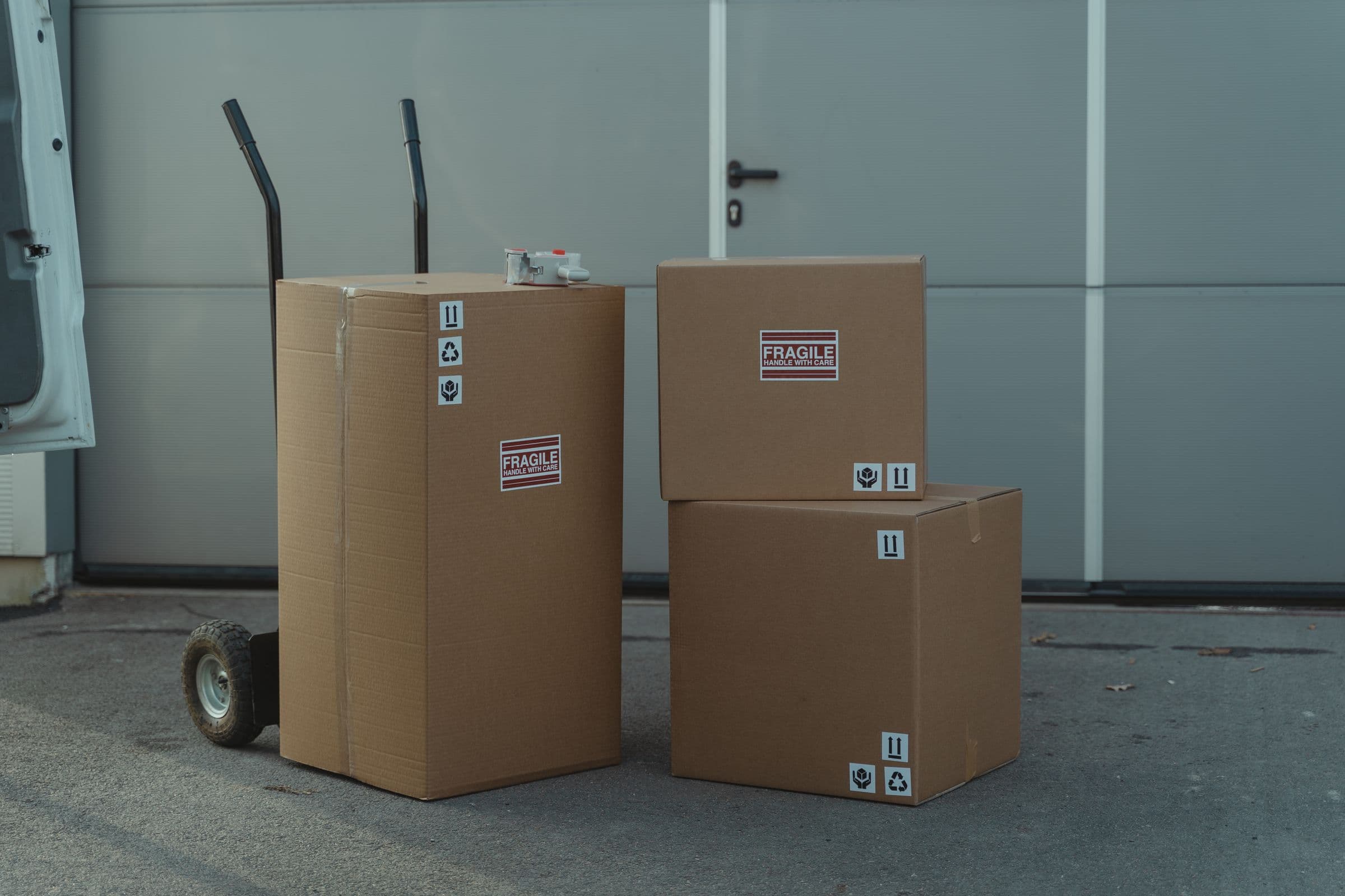 Sealed cardboard shipping boxes on a dolly outside a warehouse, representative of packaged goods ready for dispatch