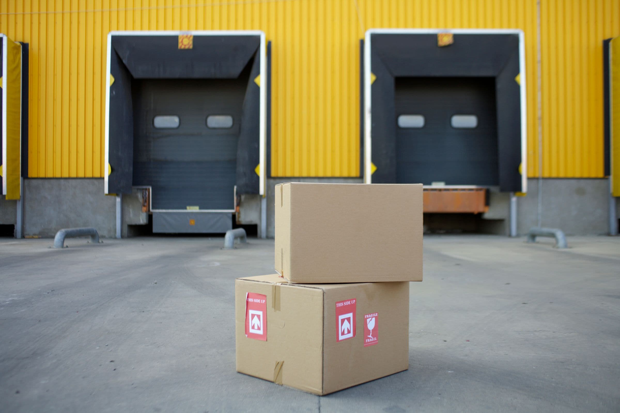 Cardboard cartons stacked at an industrial warehouse loading dock, representative of packaging moving from inspection to dispatch