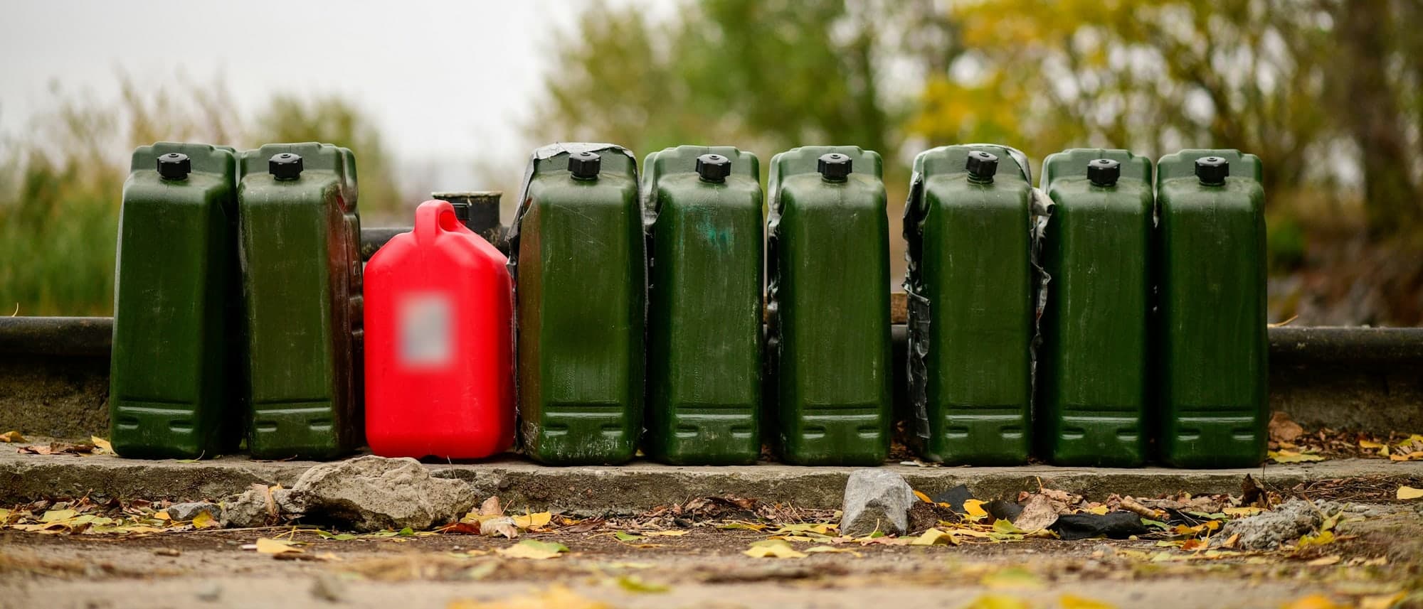 A row of identical green portable fuel containers standing against a ledge, with a single red container among them