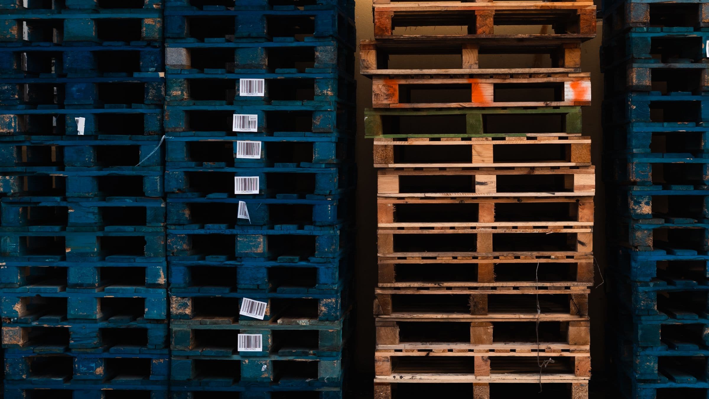 Stacked wooden pallets with barcodes in a warehouse environment, representative of the pallets tested for handling and load performance